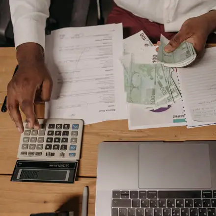 Hands tallying payments with a calculator beside a laptop