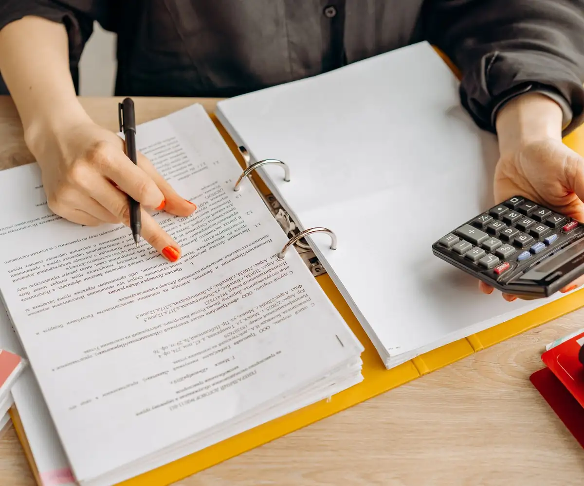 Hands checking figures in a binder with a calculator