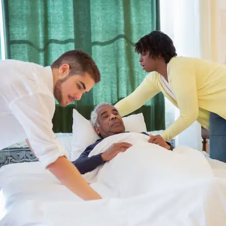 Two caregivers helping an older man settle in bed