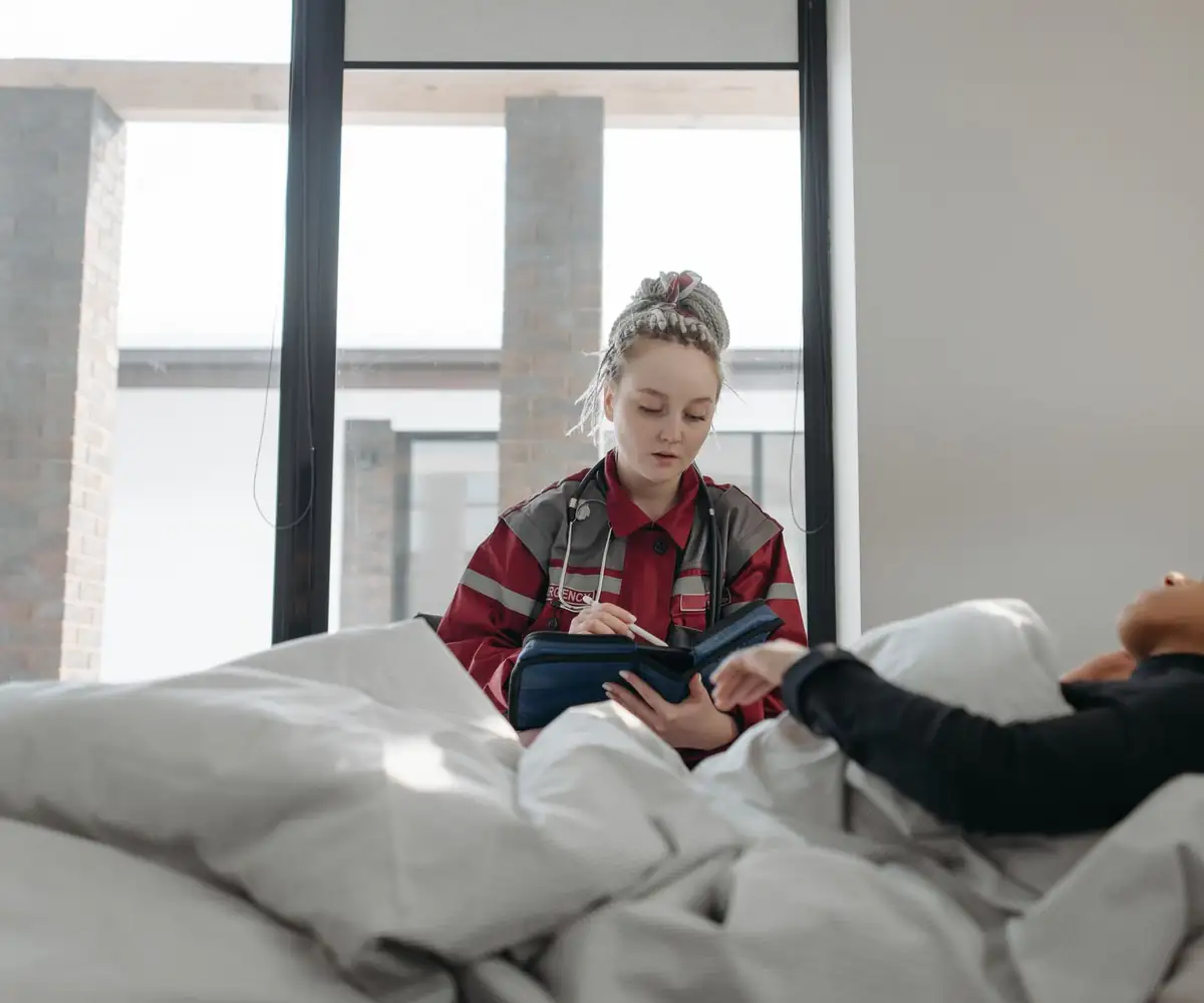 A visiting nurse writing notes at a patient’s bedside at home