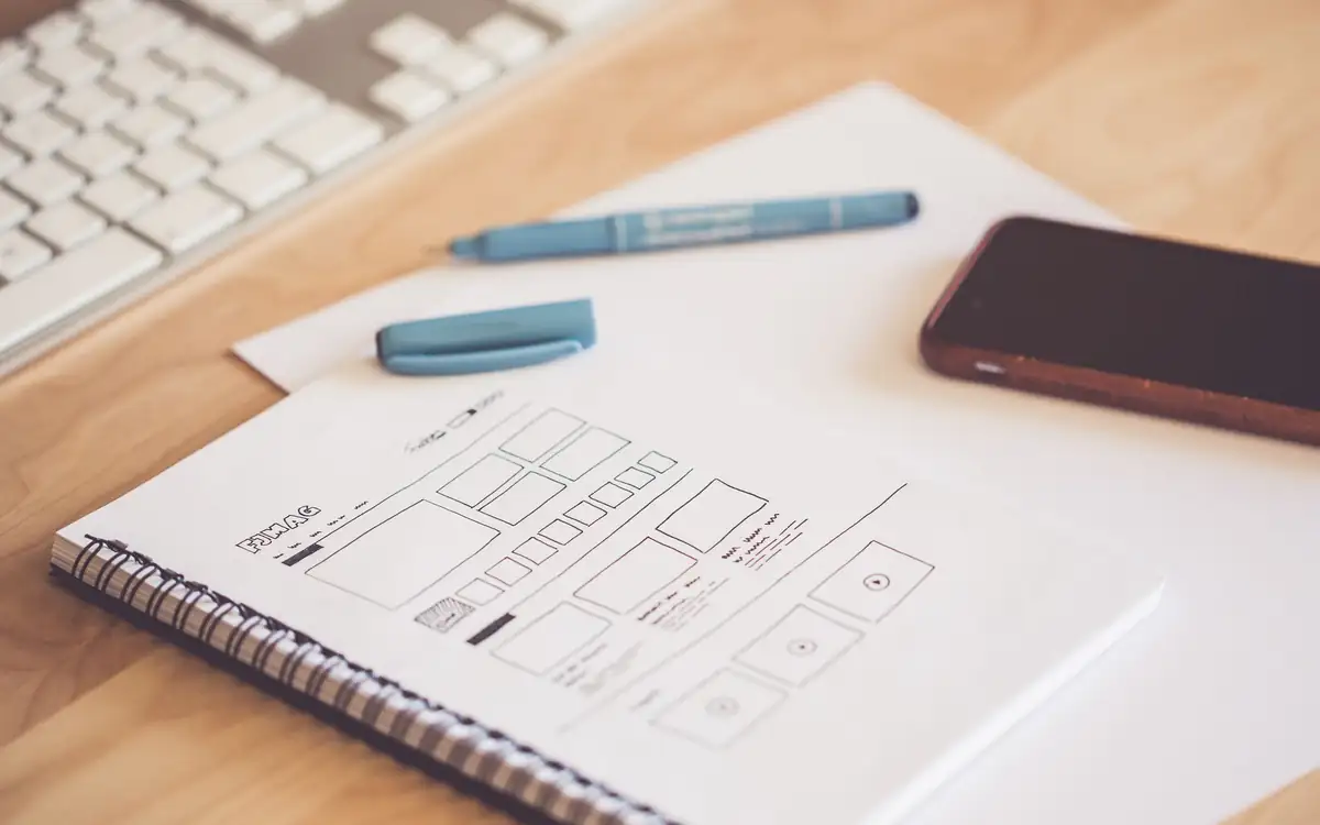 Website wireframes sketched in a notebook beside a phone