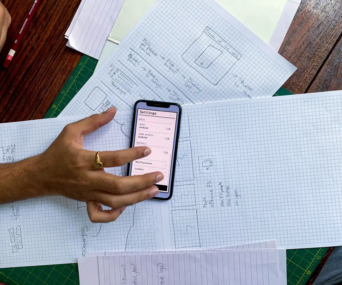 A hand holding a phone over website layout sketches